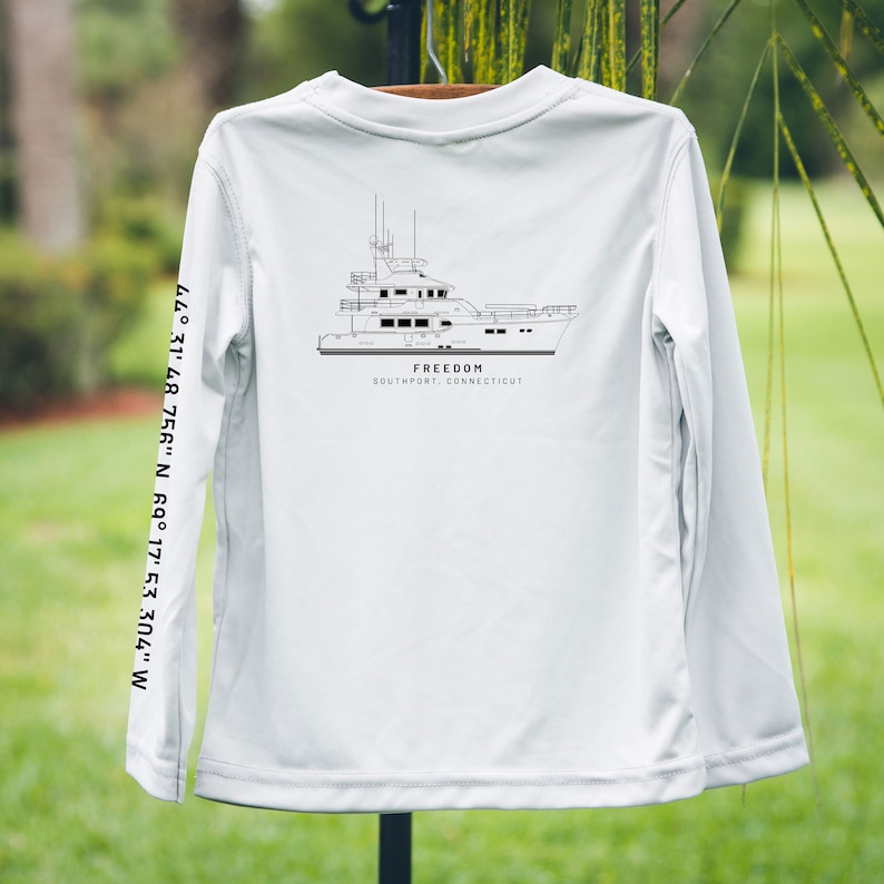 May include: White long-sleeve shirt featuring a black line drawing of a yacht. The word "FREEDOM" is above "SOUTHPORT, CONNECTICUT". Coordinates 44&deg; 31' 48.756" N 69&deg; 17' 53.304" W are printed on the sleeve.