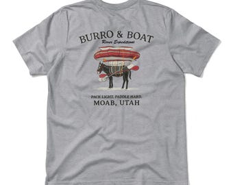 May include: A light gray t-shirt with a graphic featuring a mule carrying a boat and paddles. The text "BURRO & BOAT River Expeditions" is above the illustration, with "PACK LIGHT. PADDLE HARD. MOAB, UTAH" below.
