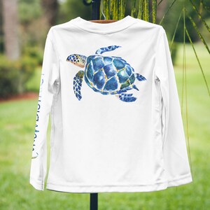 May include: White long-sleeved shirt with a blue and green watercolour sea turtle design on the back.