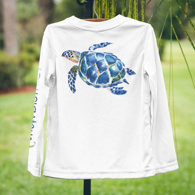 May include: White long-sleeved shirt with a blue and green watercolour sea turtle design on the back.