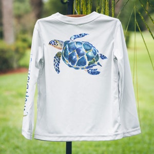 May include: White long-sleeved shirt with a blue and green sea turtle graphic on the back.