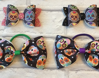 Puede incluir: Seis lazos para el pelo coloridos con un diseño de calavera de azúcar. Los lazos están hechos de tela negra con calaveras de azúcar y flores coloridas. Los lazos están atados con gomas elásticas de diferentes colores.