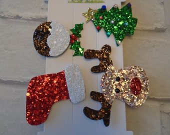 Puede incluir: Un conjunto de seis pinzas para el pelo con temática navideña que incluyen una media, un reno, un árbol de Navidad, una rama de acebo y dos diseños diferentes de pudín navideño. Las pinzas están hechas de purpurina y están empaquetadas en una tarjeta blanca con el texto "Sandi's Mini Styles".