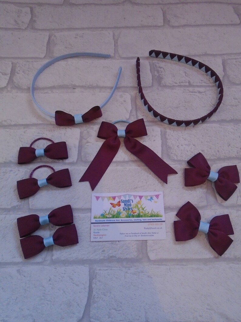 May include: An assortment of burgundy and light blue hair accessories, including headbands, hair ties, and bow clips. The headbands have a solid light blue band with a burgundy bow, and a burgundy headband with light blue triangles. The hair ties and clips feature burgundy bows with light blue centers.