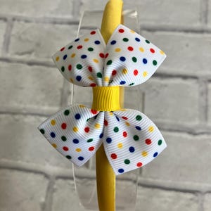 May include: Yellow headband with a white bow decorated with colorful polka dots.