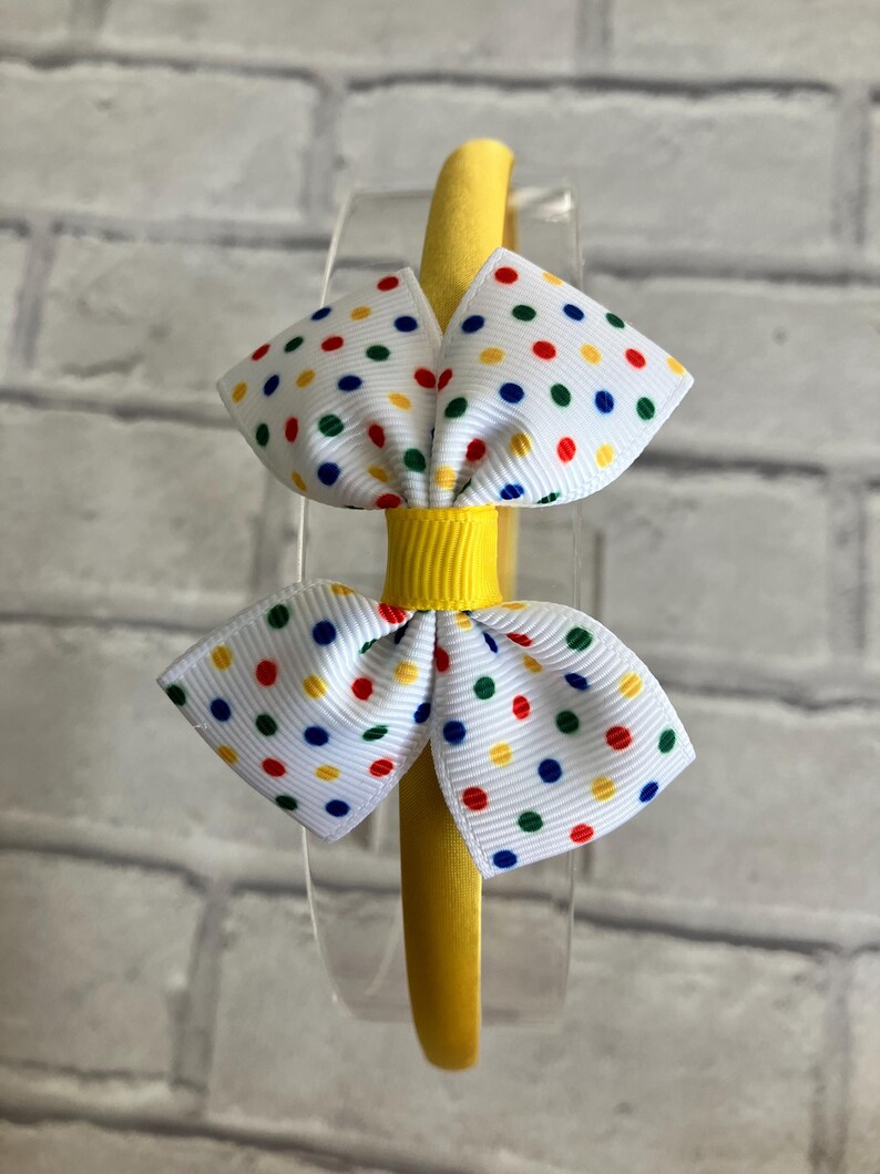 May include: Yellow headband with a white bow decorated with colorful polka dots.