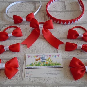 May include: A collection of red hair accessories, including headbands, bows, and ponytail holders, with white accents. The accessories are arranged on a light-colored brick background. A business card is also present.
