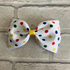 May include: A white bow with red, yellow, blue, and green polka dots. The bow is tied with a yellow ribbon.