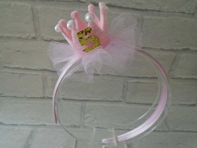 Puede incluir: Diadema rosa con una corona de fieltro rosa y el n&uacute;mero 5 en purpurina dorada. La corona tiene detalles de perlas blancas y un lazo de tul.