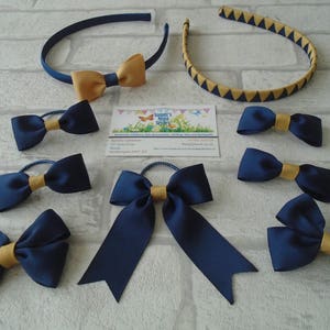 May include: A collection of navy blue and gold hair accessories, including headbands and bow-tie hair ties. One headband is navy blue with a gold bow, and the other is gold with navy blue triangles. The hair ties have a navy blue bow with a gold center.