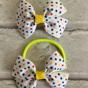 May include: Two neon yellow hair ties with white bows featuring colorful polka dots. The bows have a yellow center.