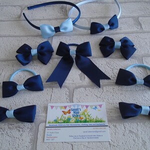 May include: An assortment of navy blue and light blue hair accessories, including headbands, bows, and hair ties. The bows have a contrasting light blue center. A business card with the text "Sandi's Mini Styles" is also visible.