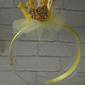 Puede incluir: Diadema de brillantina amarilla con una corona amarilla y el n&uacute;mero 19 en ella. La corona est&aacute; decorada con diamantes de imitaci&oacute;n.