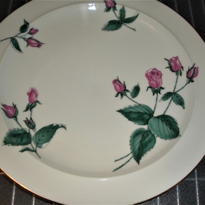 May include: A white ceramic dinner plate with a gold rim features a delicate floral design of pink roses and green leaves.