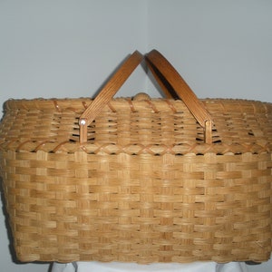 May include: A woven wicker basket with two wooden handles. The basket is oval shaped and has a light brown color.
