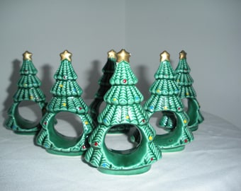 Könnte beinhalten: Set aus sechs Serviettenringen in Form von Weihnachtsbäumen aus Keramik. Jeder grüne Baum hat einen goldenen Stern und bunte Punkte. Die Serviettenringe haben eine kreisförmige Öffnung.
