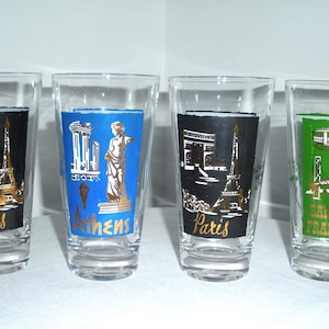 May include: Set of four vintage clear drinking glasses with colorful city-themed designs. Each glass features a different city: Paris, Athens, and San Francisco. The designs include landmarks like the Eiffel Tower and the Golden Gate Bridge.