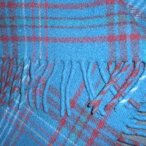 May include: A blue plaid throw blanket with fringe on the bottom edge. The blanket has a red, white, and green plaid pattern.