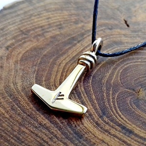 May include: A gold-colored Mjolnir pendant necklace with a black cord. The pendant features a small rune carved into the hammer head.