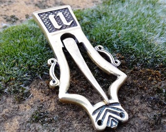 May include: A silver-colored metal clasp with an ornate design. The clasp has a pointed end and two loops on the side. The top of the clasp has a rectangular plate with the letter "II" engraved on it.