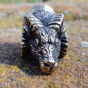 May include: A detailed silver metal wolf head with a textured surface and a raised design. The wolf head is facing forward with its mouth closed.