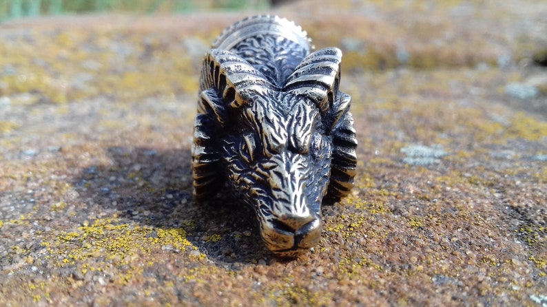 May include: A detailed silver metal wolf head with a textured surface and a raised design. The wolf head is facing forward with its mouth closed.