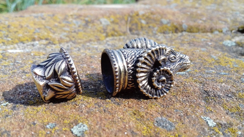 May include: Two silver metal bottle stoppers, one with a ram's head design and the other with a floral design.