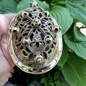 Może przedstawiać: Złota metalowa broszka z celtyckim wzorem węzł&oacute;w, o okrągłym kształcie i sześciu ozdobnych kulkach. Broszka ma skomplikowany i szczeg&oacute;łowy wz&oacute;r.
