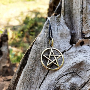 May include: A gold-colored pentagram pendant hangs from a black cord against a rustic wooden background.