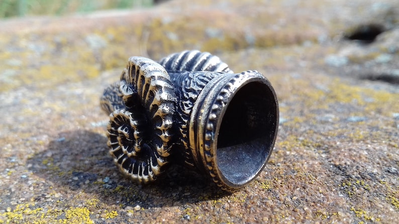 May include: A silver-colored metal thimble with a detailed spiral design on the side. The thimble has a smooth, round opening at the top.