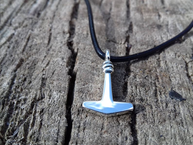 Op de afbeelding: Een zilveren Mjolnir-hanger aan een zwart leren koord. De hanger is een replica van Thor's hamer uit de Noorse mythologie.