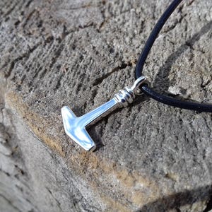 Op de afbeelding: Een zilveren hamer hanger aan een zwart leren koord. De hanger is simpel van ontwerp met een afgeronde kop en een rechte steel.
