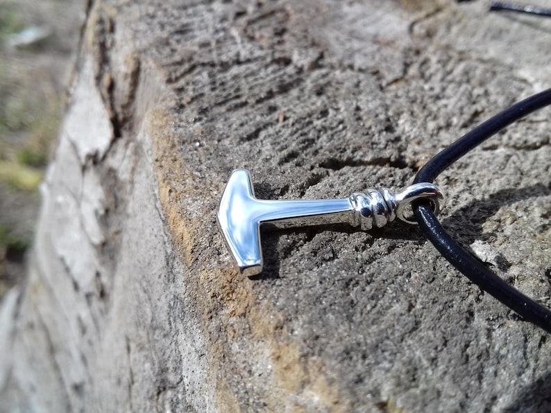Op de afbeelding: Een zilveren Mjolnir-hanger aan een zwart leren koord. De hanger is een replica van Thor's hamer uit de Noorse mythologie.