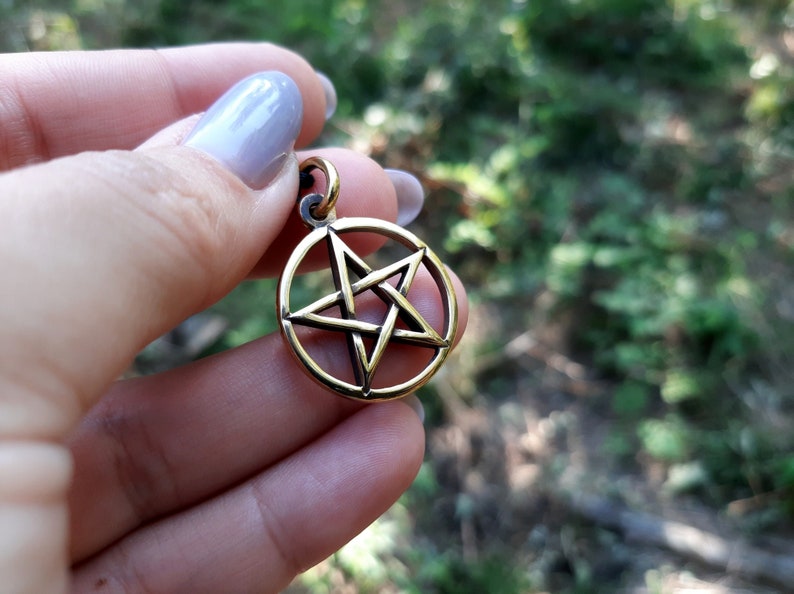 May include: A gold-toned pendant featuring a five-pointed star, also known as a pentagram, within a circle.