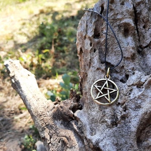 May include: A gold-toned pentagram pendant necklace on a black cord, hanging from a weathered tree branch.