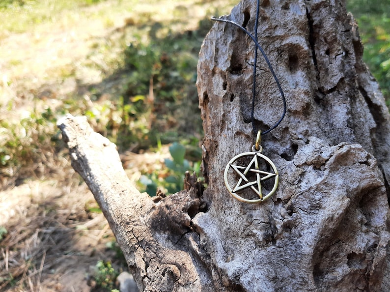 May include: A gold-toned pentagram pendant necklace on a black cord, hanging from a weathered tree branch.