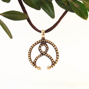 May include: A bronze pendant necklace with a circular design featuring a stylized figure with dots around the edge.