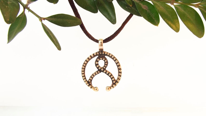 May include: A bronze pendant necklace with a circular design featuring a stylized figure with dots around the edge.