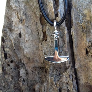 Op de afbeelding: Een zilveren hanger in de vorm van een hamer hangt aan een zwart leren koord. De hanger is een Noors symbool voor Thors hamer, Mjolnir.