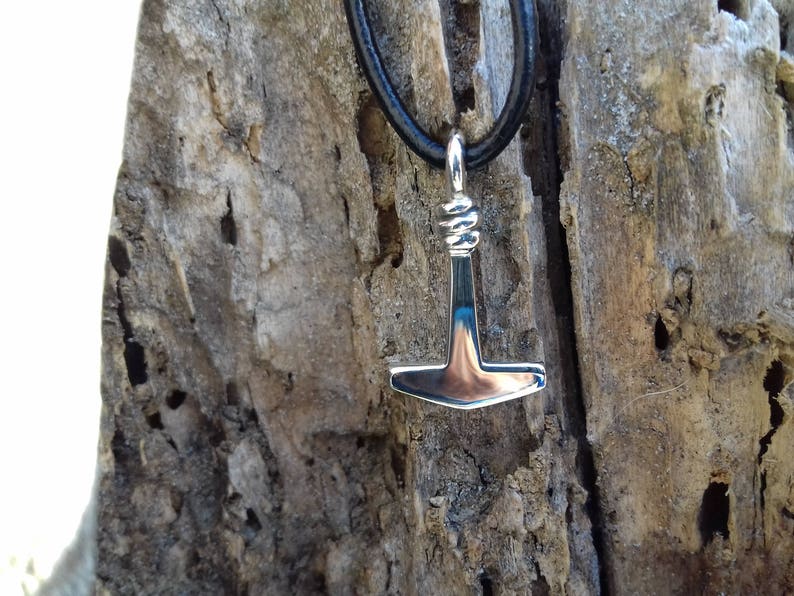 Op de afbeelding: Een zilveren hanger in de vorm van een hamer hangt aan een zwart leren koord. De hanger is een Noors symbool voor Thors hamer, Mjolnir.