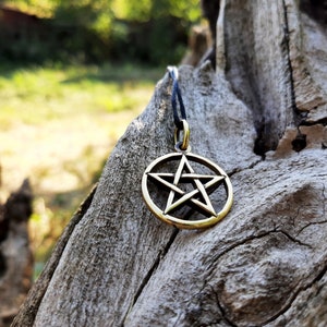 May include: A gold-colored pentagram pendant necklace with a black cord. The pendant is a five-pointed star inside a circle, a symbol of protection and balance.
