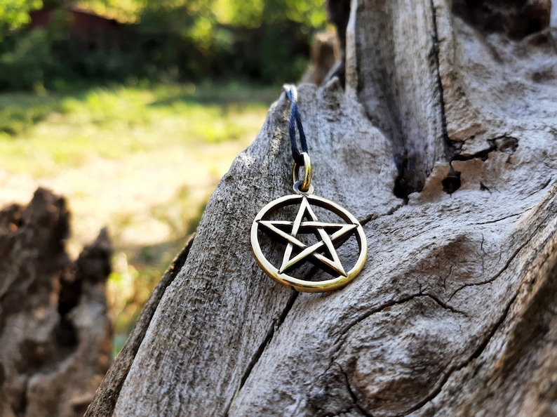 May include: A gold-colored pentagram pendant necklace with a black cord. The pendant is a five-pointed star inside a circle, a symbol of protection and balance.