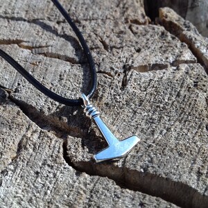 Op de afbeelding: Een zilveren Mjolnir-hanger aan een zwart leren koord. De hanger is een replica van Thor's hamer uit de Noorse mythologie.