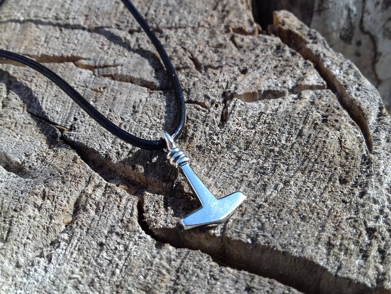 Op de afbeelding: Een zilveren Mjolnir-hanger aan een zwart leren koord. De hanger is een replica van Thor's hamer uit de Noorse mythologie.