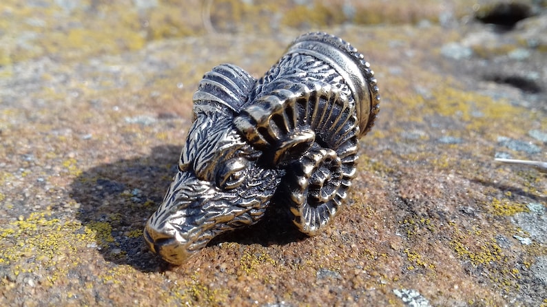 May include: A silver-colored metal ram head with detailed horns and a textured surface.