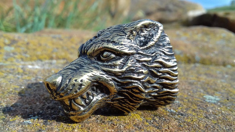 May include: A detailed bronze wolf head sculpture with a snarling expression. The sculpture is textured and has a realistic appearance.