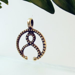 May include: A gold-toned metal pendant with a circular design featuring a stylized figure with a beaded border.