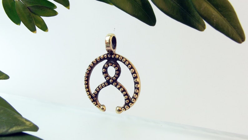 May include: A gold-toned metal pendant with a circular design featuring a stylized figure with a beaded border.