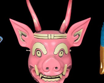 May include: Three colourful Japanese masks against a black backdrop. The masks include a blue demon mask with red accents, a pink pig-like mask, and a gold-coloured mask with blue hair.