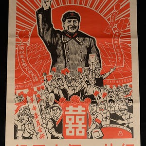 May include: A vintage Chinese propaganda poster in red and black. It depicts a man with his arm raised, surrounded by a crowd. The poster includes Chinese text and a red sunburst design.